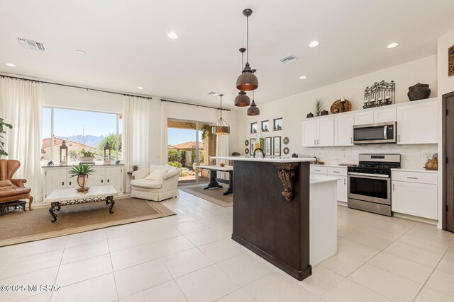 kitchen with white cabinetry, tasteful backsplash, appliances with stainless steel finishes, an island with sink, and pendant lighting