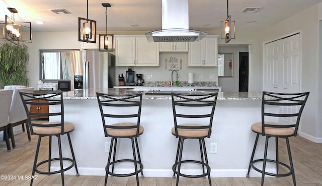 kitchen featuring a breakfast bar, white cabinetry, stainless steel refrigerator with ice dispenser, light stone counters, and island exhaust hood