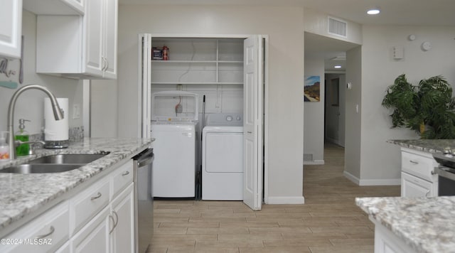 kitchen with sink, stainless steel dishwasher, independent washer and dryer, light stone countertops, and white cabinets