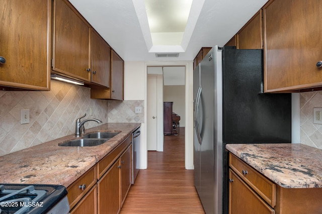 kitchen with sink, light hardwood / wood-style flooring, stainless steel appliances, light stone counters, and decorative backsplash