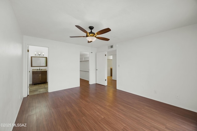 unfurnished bedroom with connected bathroom, a walk in closet, dark hardwood / wood-style flooring, a closet, and ceiling fan