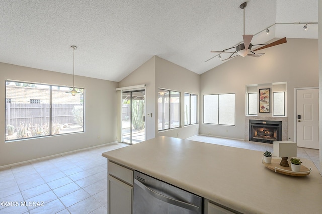 kitchen featuring a textured ceiling, dishwasher, a tile fireplace, pendant lighting, and white cabinets