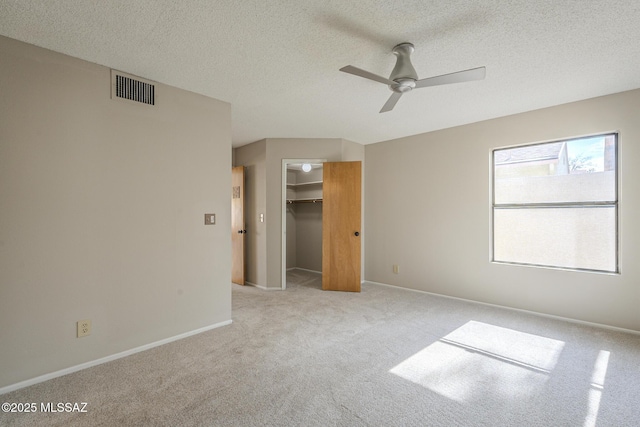 unfurnished bedroom featuring a spacious closet, ceiling fan, light carpet, a textured ceiling, and a closet