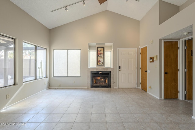 unfurnished living room with a tile fireplace, rail lighting, light tile patterned floors, and high vaulted ceiling