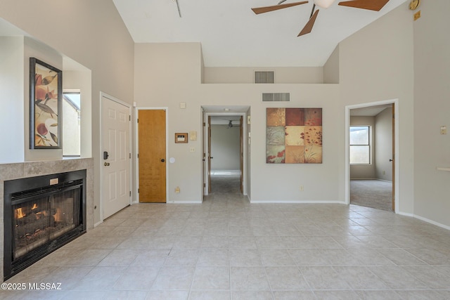 unfurnished living room with a tiled fireplace, light tile patterned floors, high vaulted ceiling, and ceiling fan