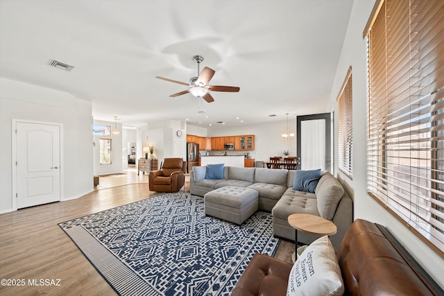 living room with ceiling fan with notable chandelier and light hardwood / wood-style flooring