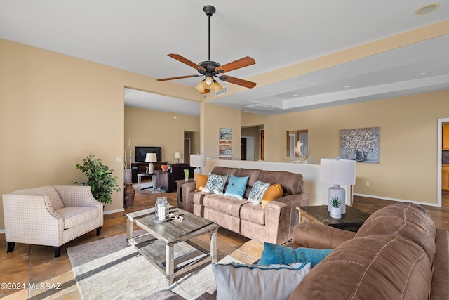 living room featuring ceiling fan, visible vents, baseboards, and a tray ceiling