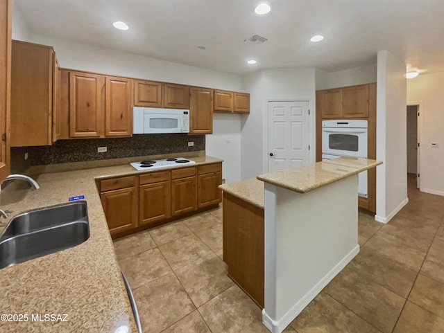 kitchen featuring sink, backsplash, a center island, light stone counters, and white appliances