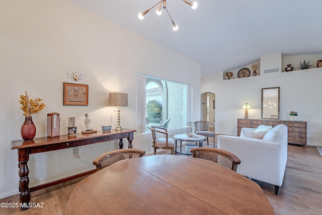 dining area featuring a notable chandelier, high vaulted ceiling, and light hardwood / wood-style flooring