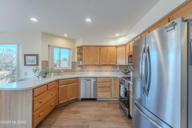 kitchen with sink, light hardwood / wood-style flooring, backsplash, stainless steel appliances, and kitchen peninsula