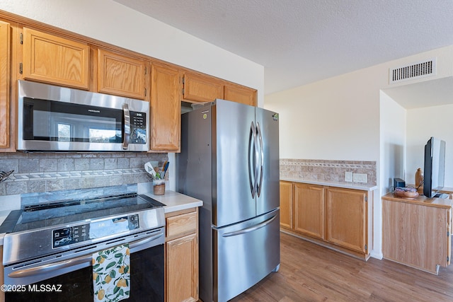 kitchen with appliances with stainless steel finishes, a textured ceiling, light hardwood / wood-style flooring, and backsplash