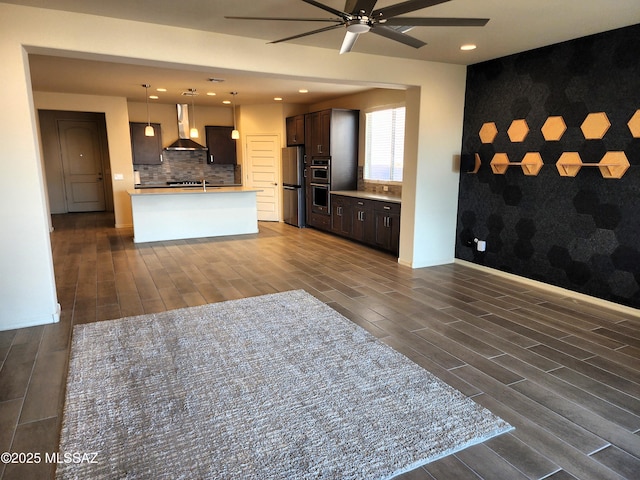 kitchen with appliances with stainless steel finishes, pendant lighting, tasteful backsplash, a center island with sink, and wall chimney range hood