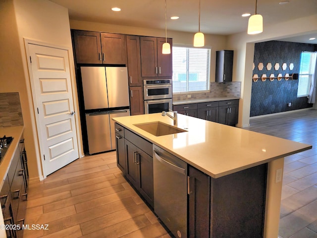 kitchen featuring sink, dark brown cabinets, stainless steel appliances, a kitchen island with sink, and decorative backsplash