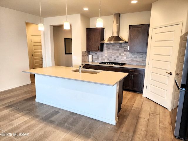 kitchen featuring sink, hanging light fixtures, a kitchen island with sink, dark brown cabinets, and wall chimney exhaust hood