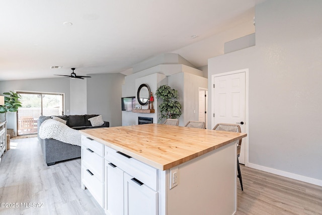 kitchen featuring a fireplace, a kitchen breakfast bar, vaulted ceiling, wooden counters, and white cabinets