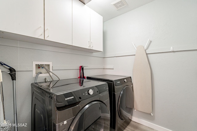 laundry area with cabinet space, baseboards, visible vents, wood finished floors, and washing machine and clothes dryer