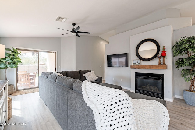 living room featuring visible vents, a glass covered fireplace, vaulted ceiling, ceiling fan, and light wood-type flooring