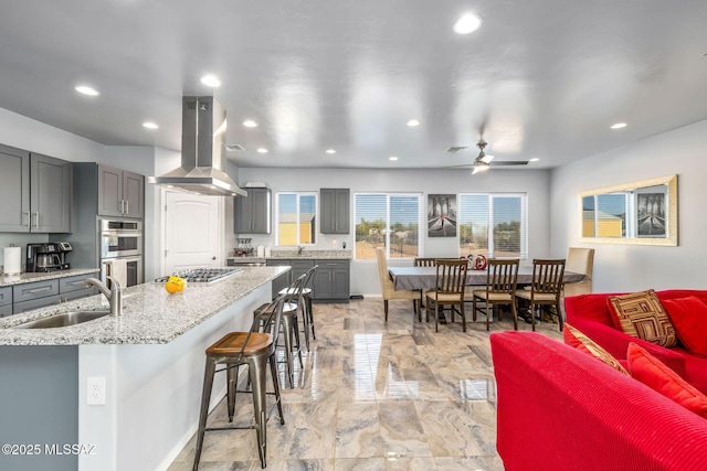 kitchen featuring gray cabinets, a breakfast bar, island range hood, sink, and stainless steel appliances