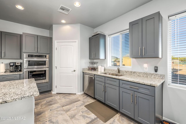 kitchen with light stone counters, appliances with stainless steel finishes, sink, and gray cabinetry