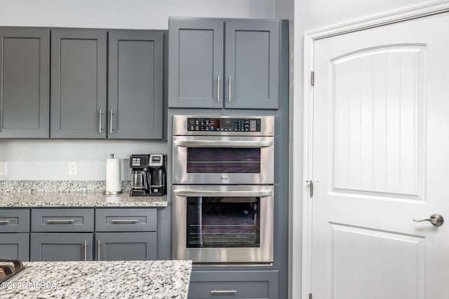 kitchen featuring gray cabinets, light stone countertops, and double oven