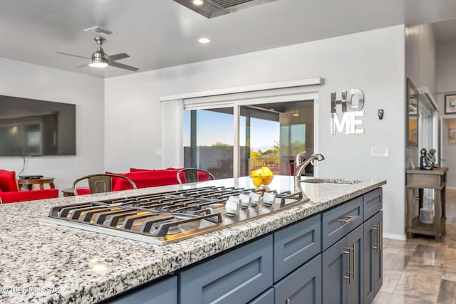 kitchen with light stone counters, sink, stainless steel gas stovetop, and ceiling fan