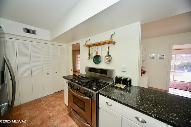 kitchen with light tile patterned flooring, appliances with stainless steel finishes, dark stone countertops, and white cabinets