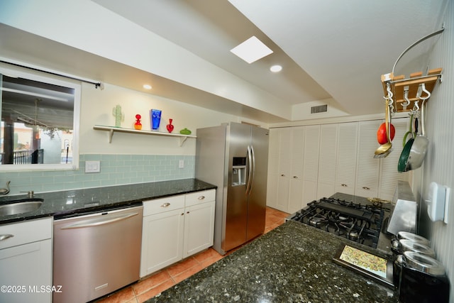 kitchen featuring white cabinetry, tasteful backsplash, stainless steel appliances, and dark stone counters