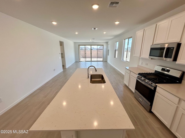 kitchen with open floor plan, stainless steel appliances, a sink, an island with sink, and visible vents