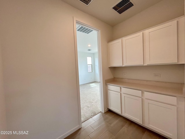 kitchen featuring light countertops, light wood-type flooring, baseboards, visible vents, and white cabinets