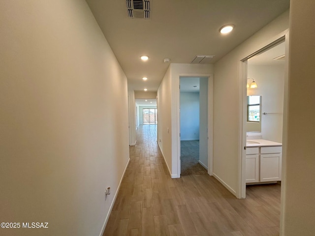 corridor featuring recessed lighting, baseboards, a sink, light wood finished floors, and visible vents