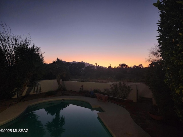 pool at dusk featuring a fenced in pool and a fenced backyard