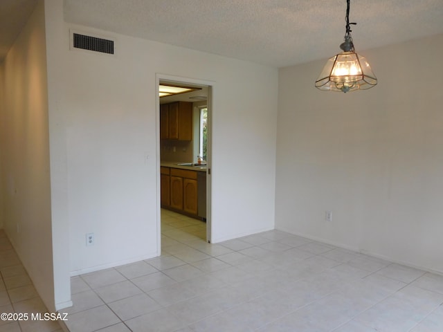 empty room with light tile patterned floors, a textured ceiling, visible vents, a sink, and baseboards