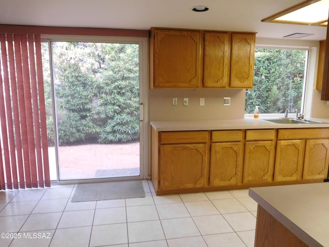 kitchen with a sink, light tile patterned floors, light countertops, and brown cabinetry