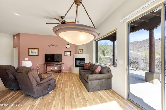 living room with vaulted ceiling, ceiling fan, a fireplace, and light hardwood / wood-style floors