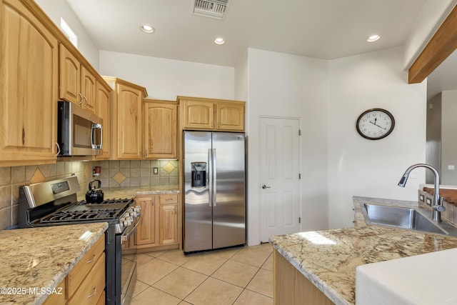 kitchen featuring sink, backsplash, stainless steel appliances, light stone countertops, and light tile patterned flooring