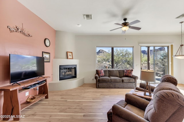 living room with ceiling fan, a large fireplace, and light hardwood / wood-style floors