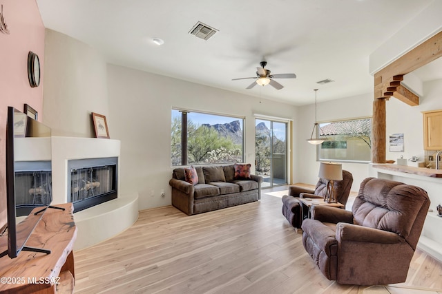 living room featuring ceiling fan, a fireplace, and light hardwood / wood-style floors