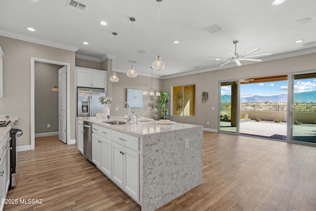 kitchen with sink, appliances with stainless steel finishes, a kitchen island with sink, white cabinetry, and a mountain view