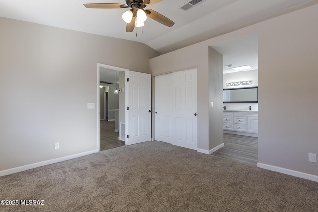 unfurnished bedroom featuring vaulted ceiling, connected bathroom, dark colored carpet, ceiling fan, and a closet