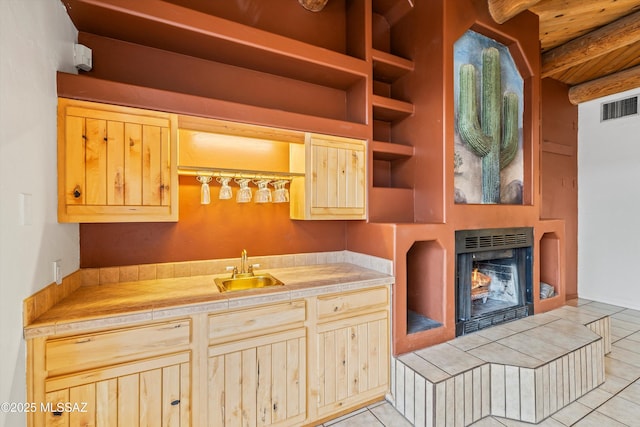 kitchen featuring built in features, sink, a tiled fireplace, tile counters, and light tile patterned floors