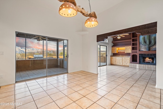 unfurnished room featuring light tile patterned flooring, ceiling fan, built in shelves, and a high ceiling