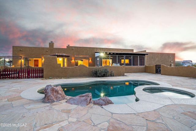 pool at dusk featuring a patio area and an in ground hot tub