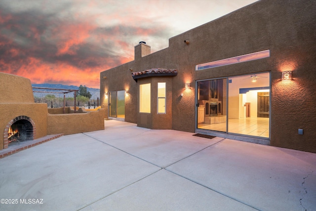 back house at dusk featuring an outdoor brick fireplace and a patio area