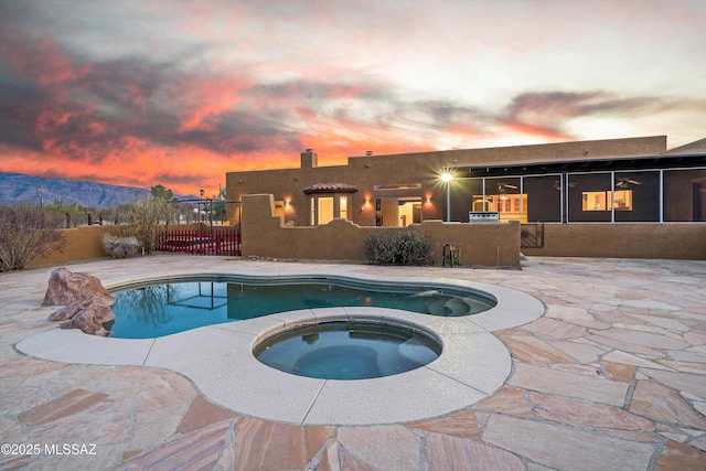 pool at dusk featuring an in ground hot tub, a mountain view, and a patio