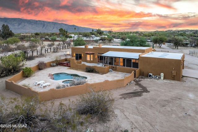 back house at dusk with an in ground hot tub, a mountain view, and a sunroom