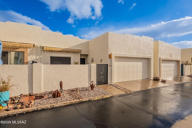 pueblo-style house with a fenced front yard, a garage, and stucco siding