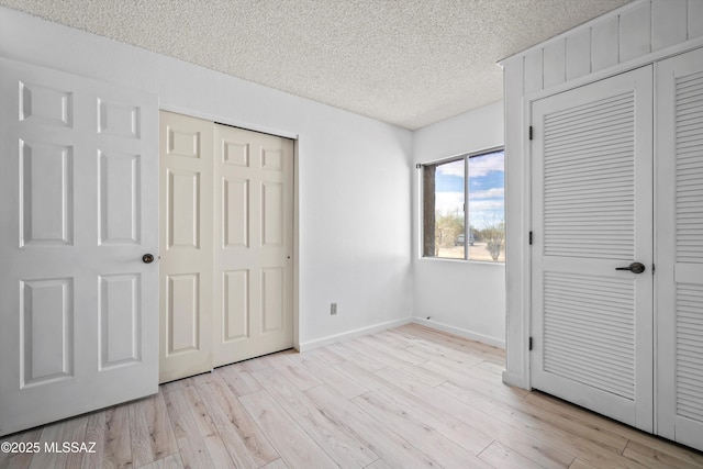 unfurnished bedroom with multiple closets, a textured ceiling, and light hardwood / wood-style floors