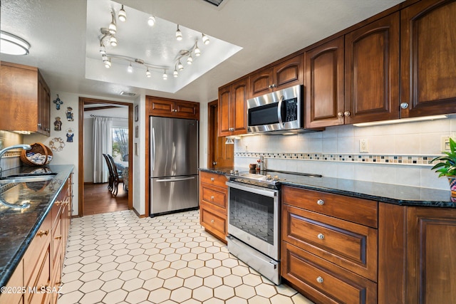 kitchen featuring dark stone counters, decorative backsplash, stainless steel appliances, a raised ceiling, and a sink