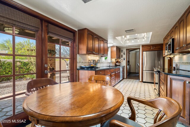 kitchen with stainless steel appliances, light floors, dark stone countertops, a sink, and decorative backsplash