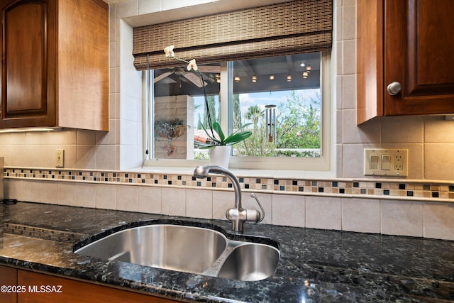 kitchen with a sink, backsplash, and dark stone countertops